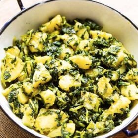 aloo methi in a enameled black rimmed small white wok on a brown jute napkin