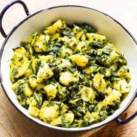 aloo methi in a enameled black rimmed small white wok on a brown jute napkin.