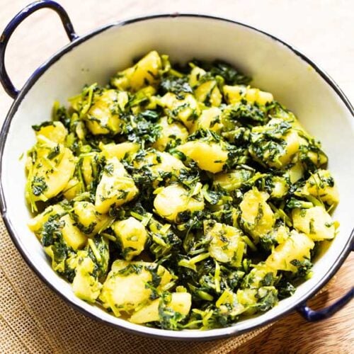 aloo methi in a enameled black rimmed small white wok on a brown jute napkin.