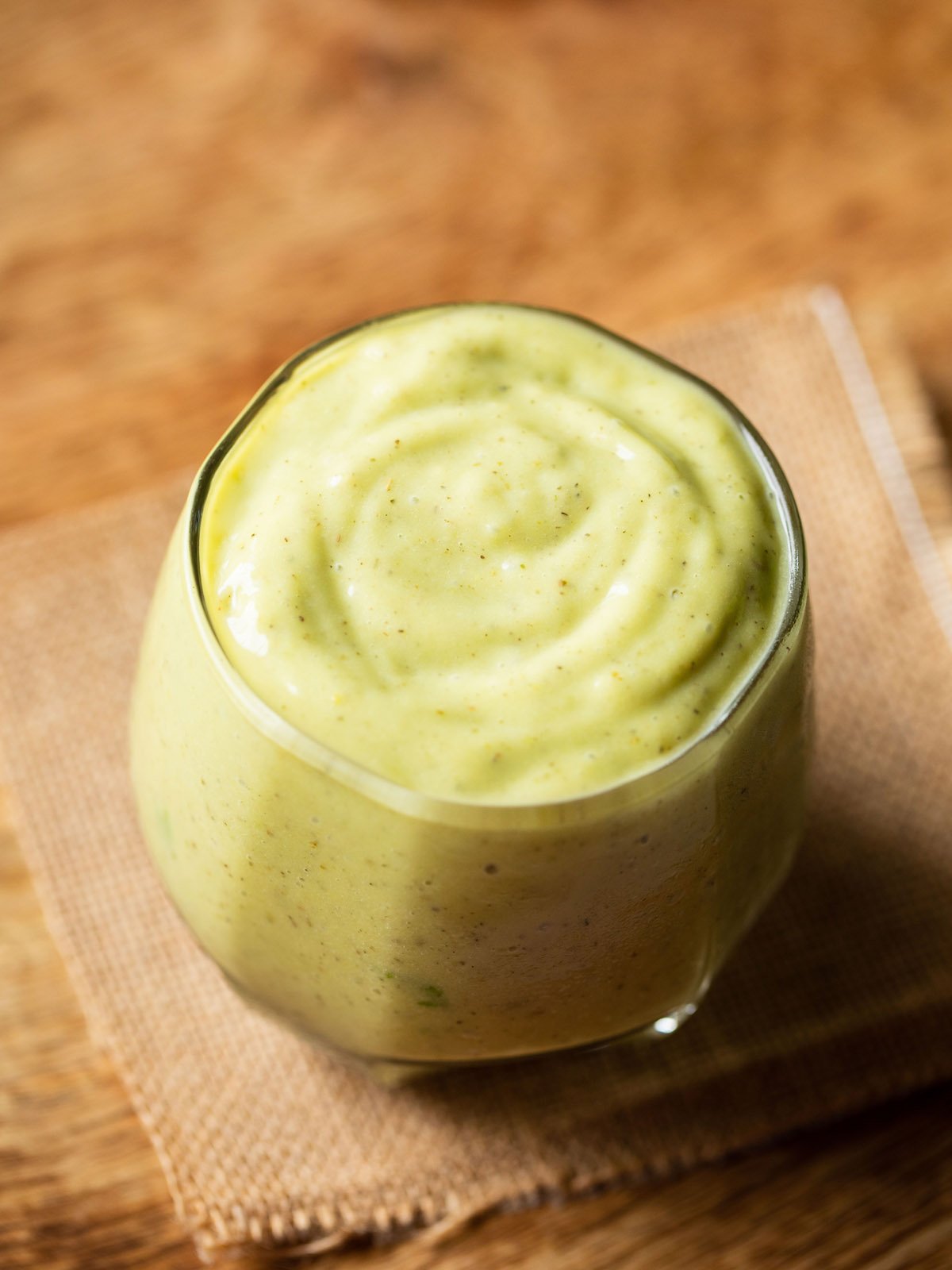 avocado milkshake in a glass on jute napkin on light brown wooden board