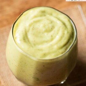 avocado milkshake in a glass on jute napkin on light brown wooden board