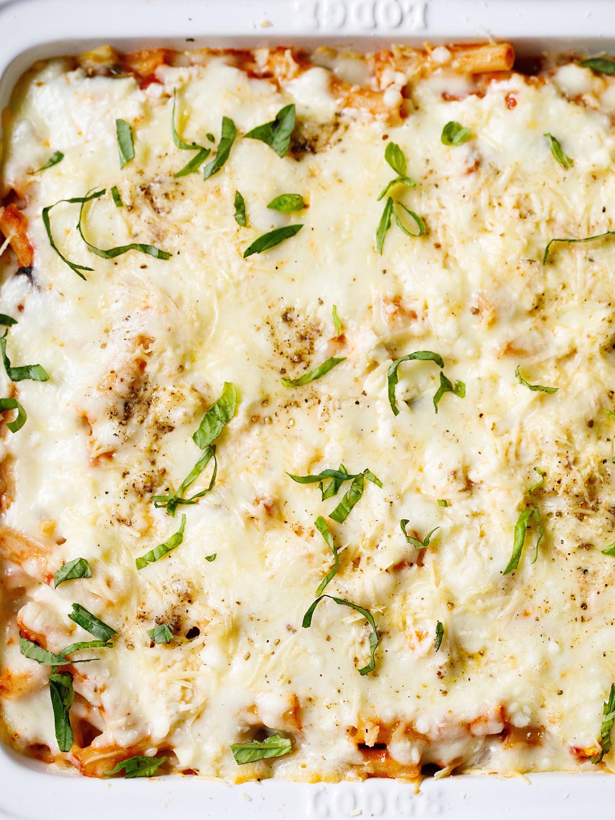 overhead shot of completed vegetarian baked ziti in a white casserole dish garnished with basil chiffonade