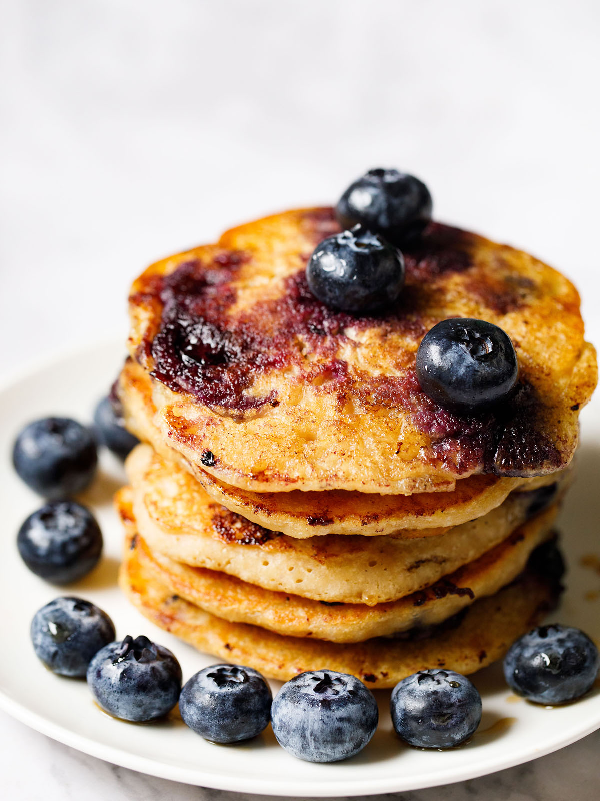 close up of stack of 5 silver dollar sized vegan blueberry pancakes on a white plate