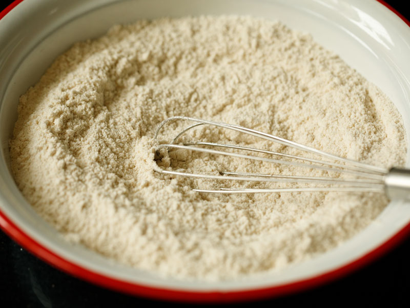 silver whisk with dry pancake batter ingredients mixed together in a red and white mixing bowl