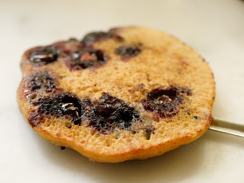 vegan blueberry pancake on a silver spatula on top of a white plate