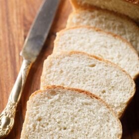 homemade bread loaf sliced with the slices placed on top of each other with an antique butter knife on a brown wooden board