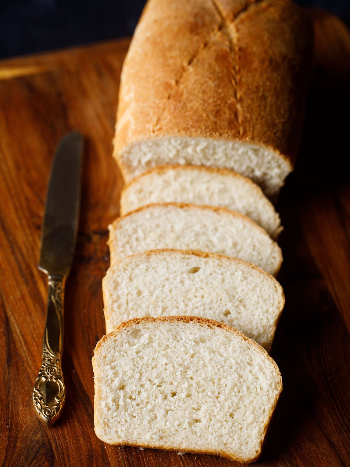 white-sandwich-bread-recipe white bread loaf sliced with the slices placed on top of each other with an antique butter knife on a brown wooden board