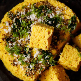 khaman dhokla squares garnished with coriander leaves and fried curry leaves and spices mixture.