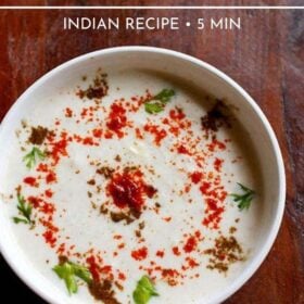 cucumber raita sprinkled with red chilli powder, roasted cumin powder and coriander leaves, served in a white bowl on a dark brown wooden board with text layover.