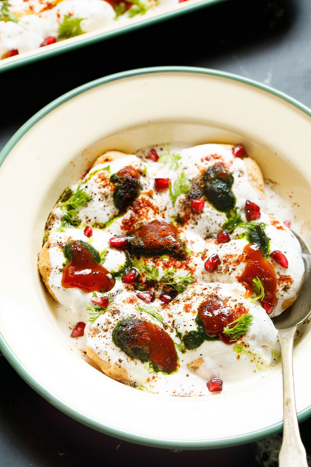 servings of homemade dahi vada with coriander and tamarind chutney, pomegranate arils, coriander leaves, ground spices and salt