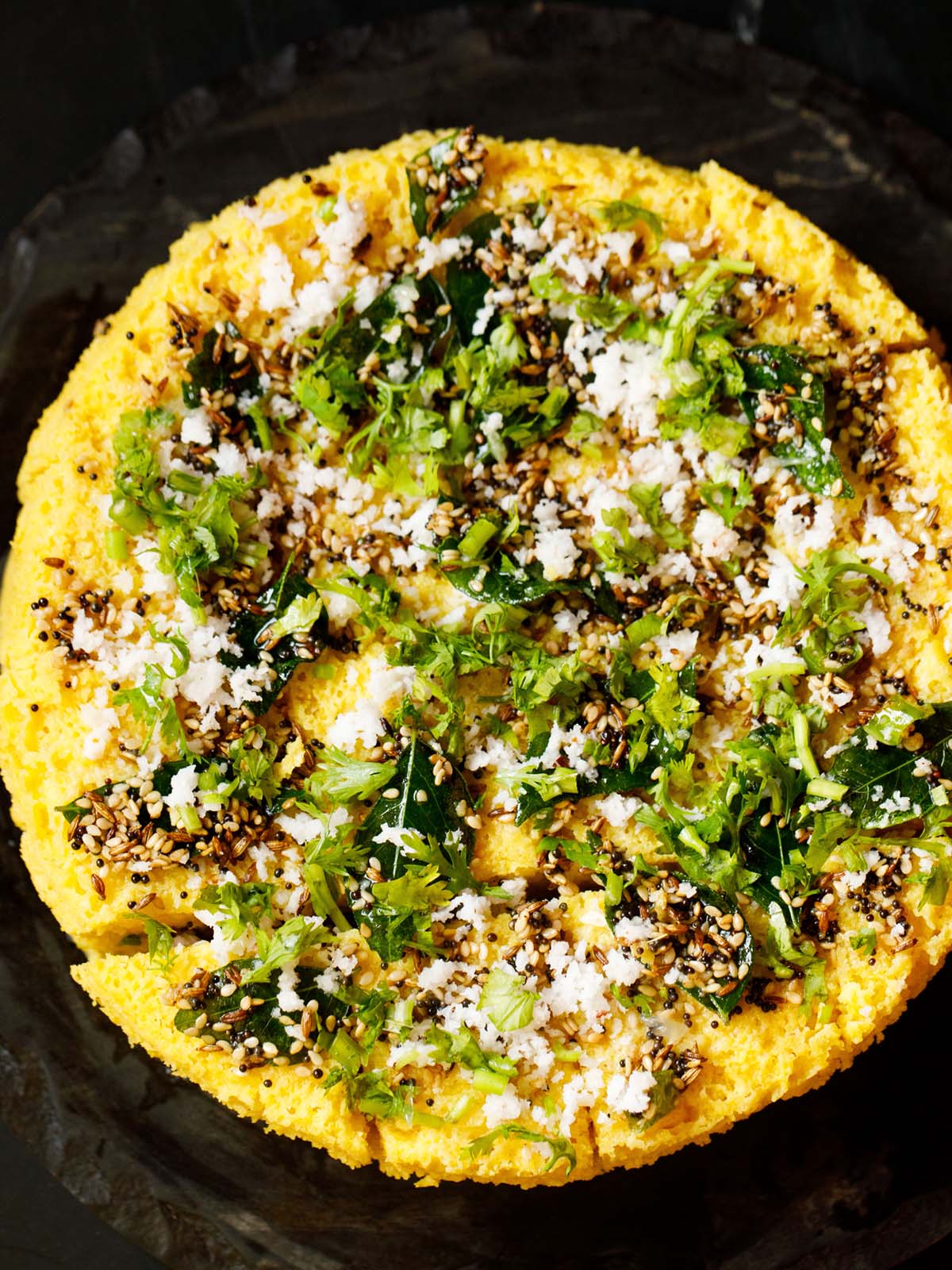 top view of the round steamed khman dhokla topped and garnished with the tempered spices, coriander leaves, and fresh grated coconut