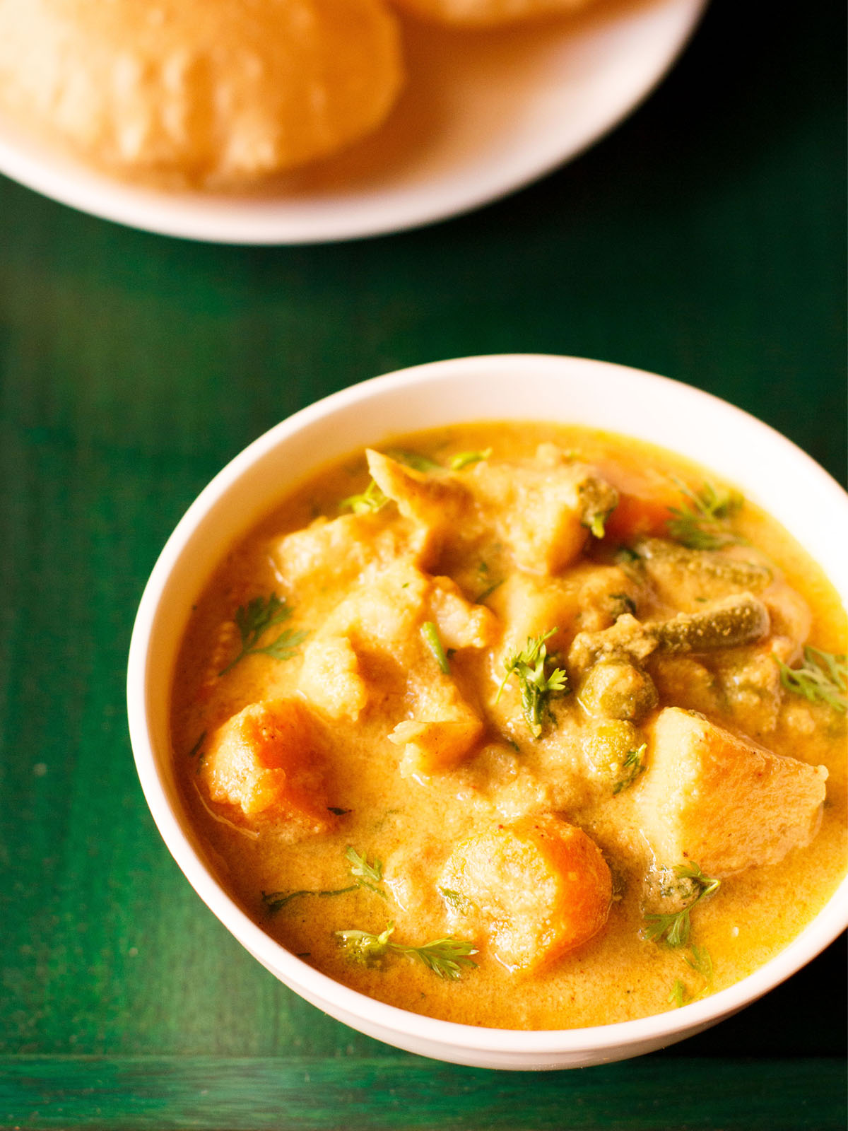 korma in a white bowl on a dark green wooden tray with a side of poori