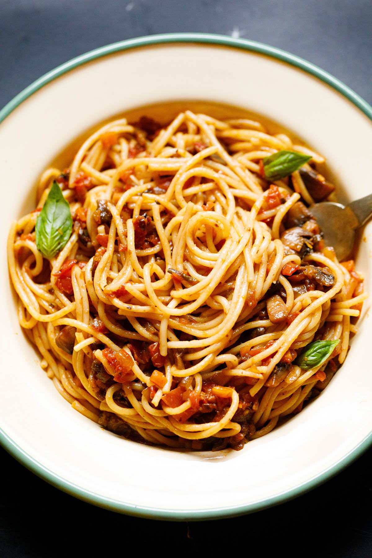 homemade spaghetti bolognese topped with fresh basil in a green rimmed cream colored enameled plate