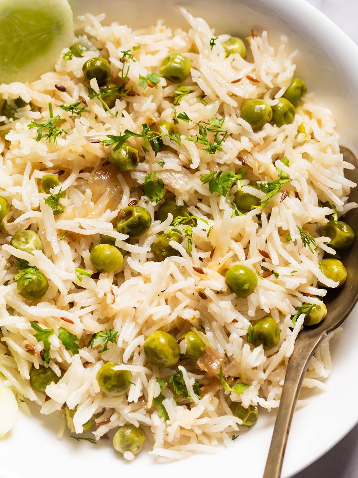 close up photo of peas pulao in a white shallow bowl with a brass spoon in the pulao