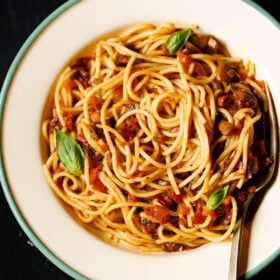 close up shot of spaghetti bolognese garnished with basil leaves in a green rimmed cream colored enameled plate with brass fork inside