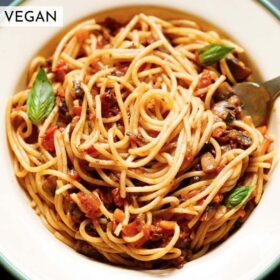 close up shot of mushroom spaghetti bolognese garnished with three basil leaves in a cream colored enameled plate with a light green rim