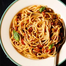 close up shot of spaghetti bolognese garnished with basil leaves in a green rimmed cream colored enameled plate with brass fork inside