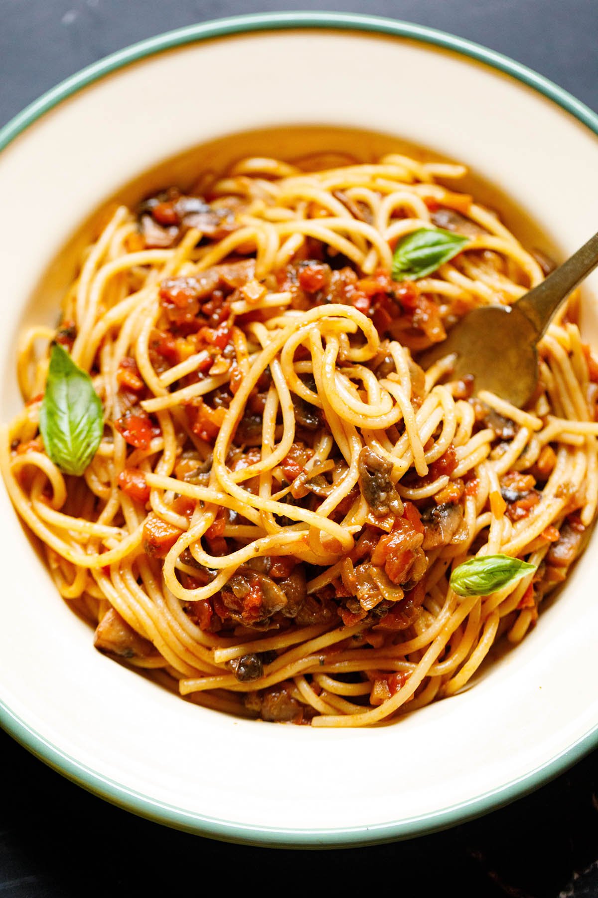 close up shot of mushroom spaghetti bolognese garnished with three basil leaves in a cream colored enameled plate with a light green rim