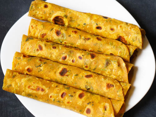 methi thepla rolls placed stacked vertically in white square plate on a dark blue black board
