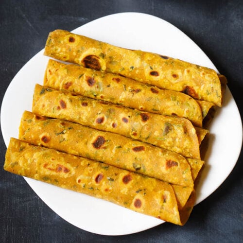 methi thepla rolls placed stacked vertically in white square plate on a dark blue black board
