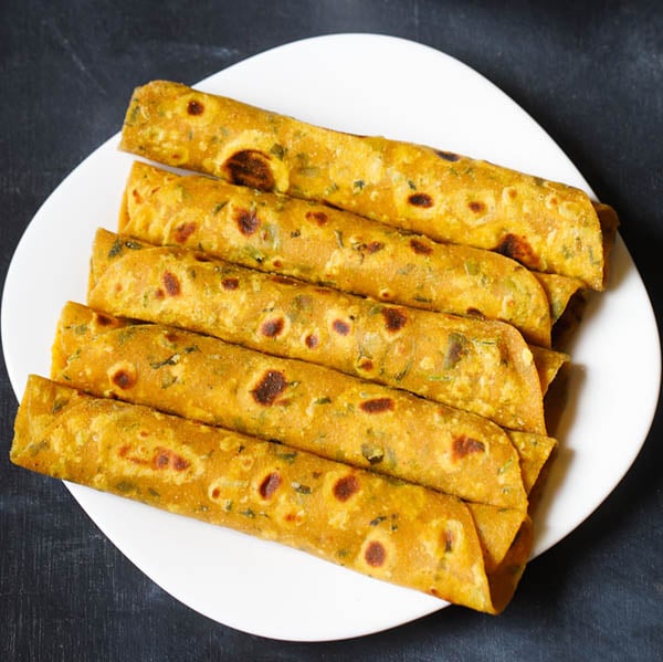 methi thepla rolls placed stacked vertically in white square plate on a dark blue black board