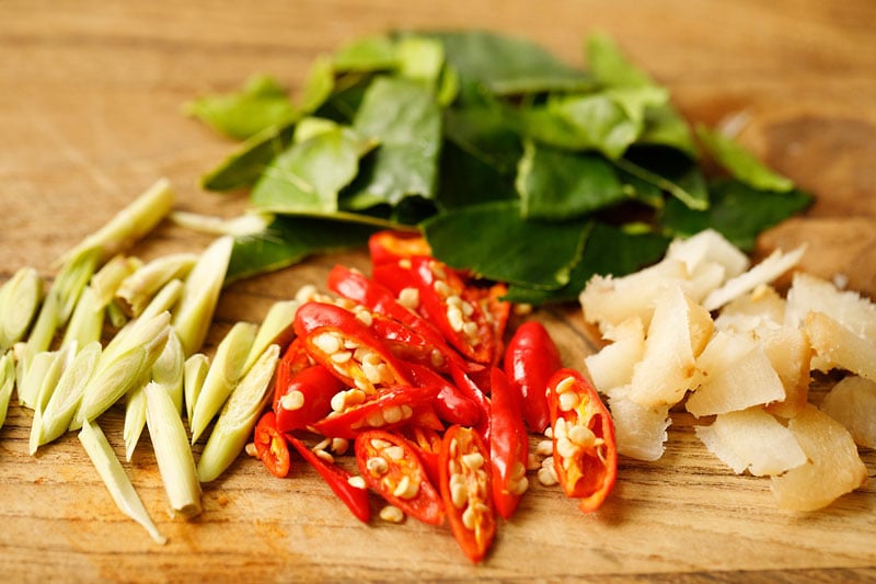 sliced lemongrass, Thai red chiles, galangal and torn kaffir lime leaves on a wooden cutting board