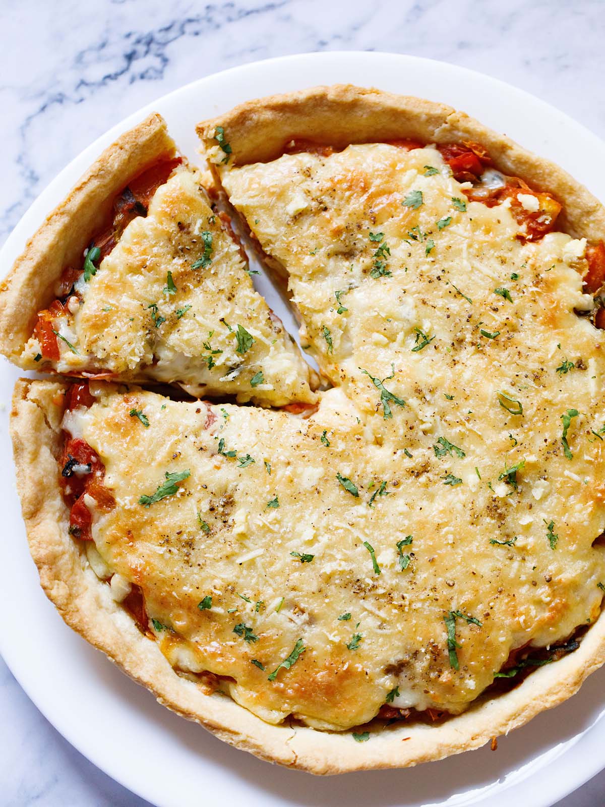 overhead shot of whole tomato pie garnished with parsley and with one slice cut and slightly askew on a white plate