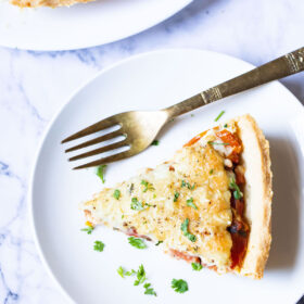 overhead shot of a slice of southern tomato pie on a white plate with a silver fork garnished with chopped parsley