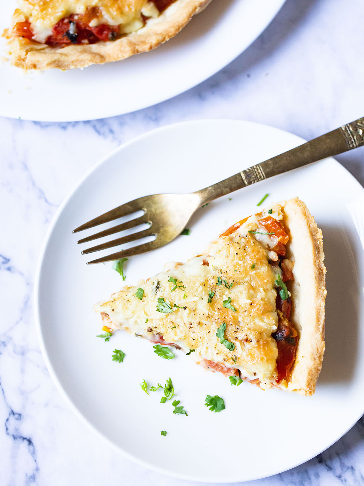 overhead shot of a slice of southern tomato pie on a white plate with a silver fork garnished with chopped parsley