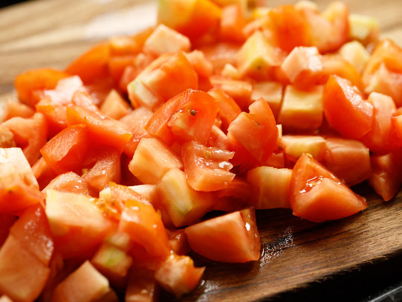 fresh tomatoes that have been cubed on a wooden cutting board