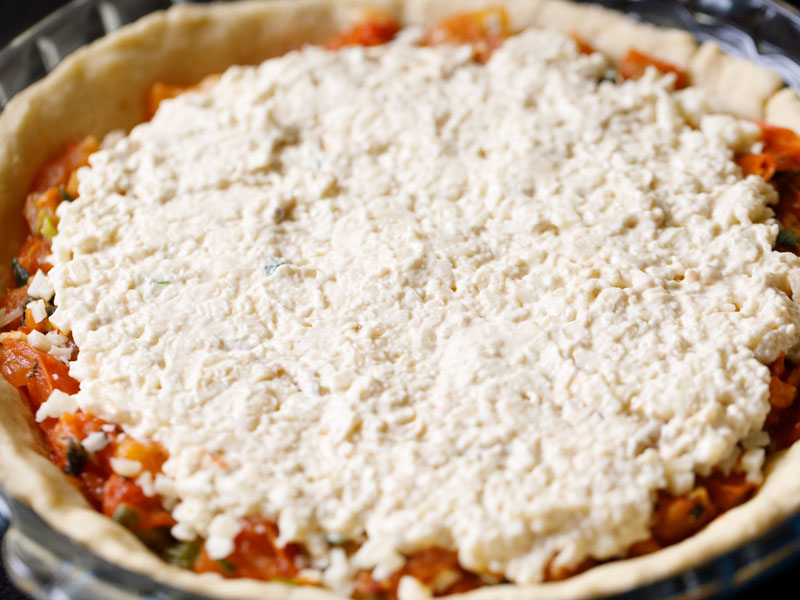 mayo and cheese filling spread out over top of southern tomato pie prior to baking