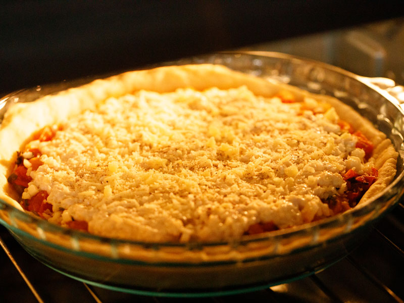 assembled southern tomato pie in a clear glass pie dish in the oven before baking