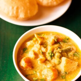 veg kurma in a white bowl on a dark green wooden tray with a side of poori