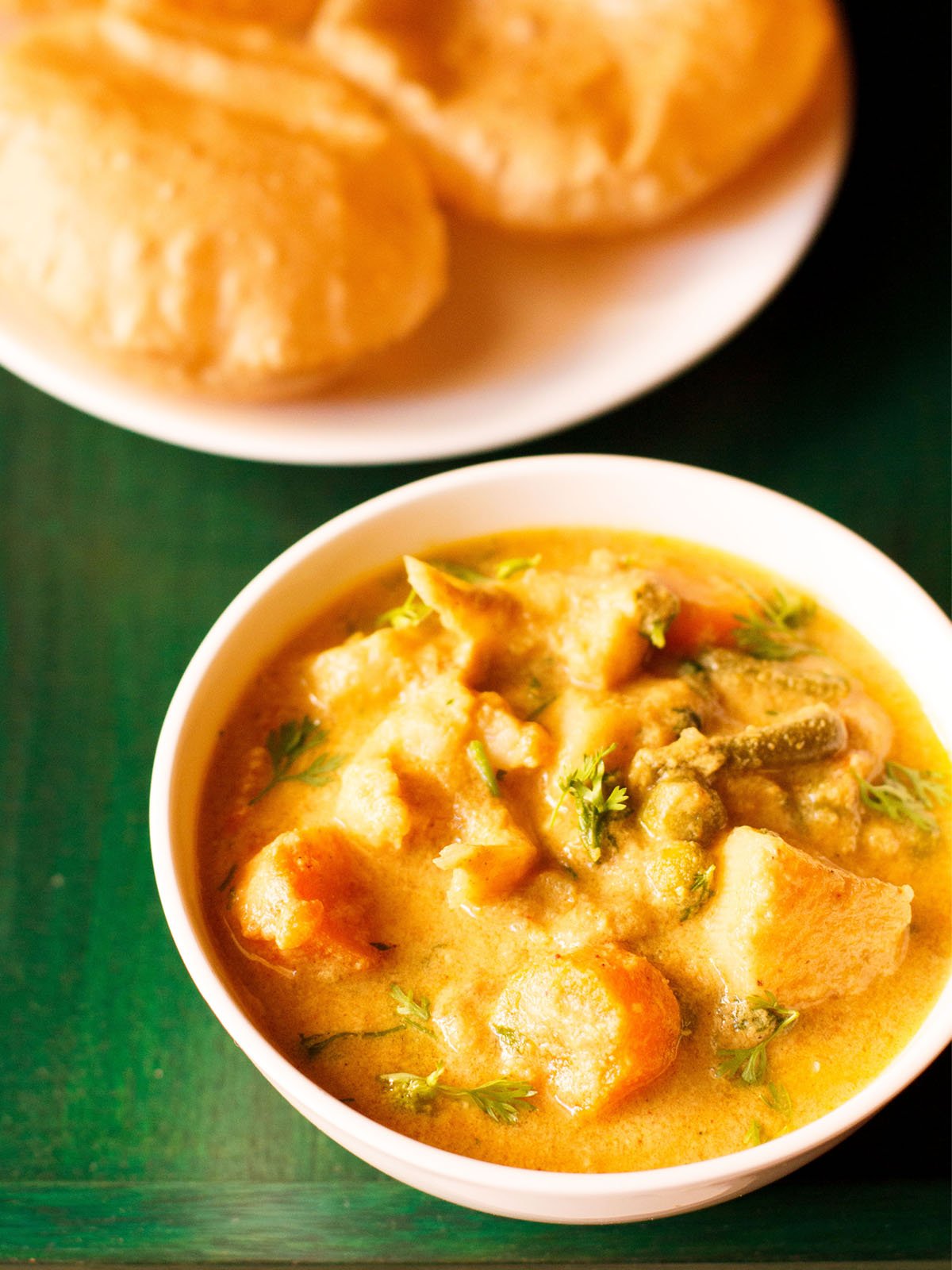 veg kurma in a white bowl on a dark green wooden tray with a side of poori