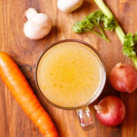 vegetable broth in a glass mug with vegetables, button mushrooms and parsley by the side