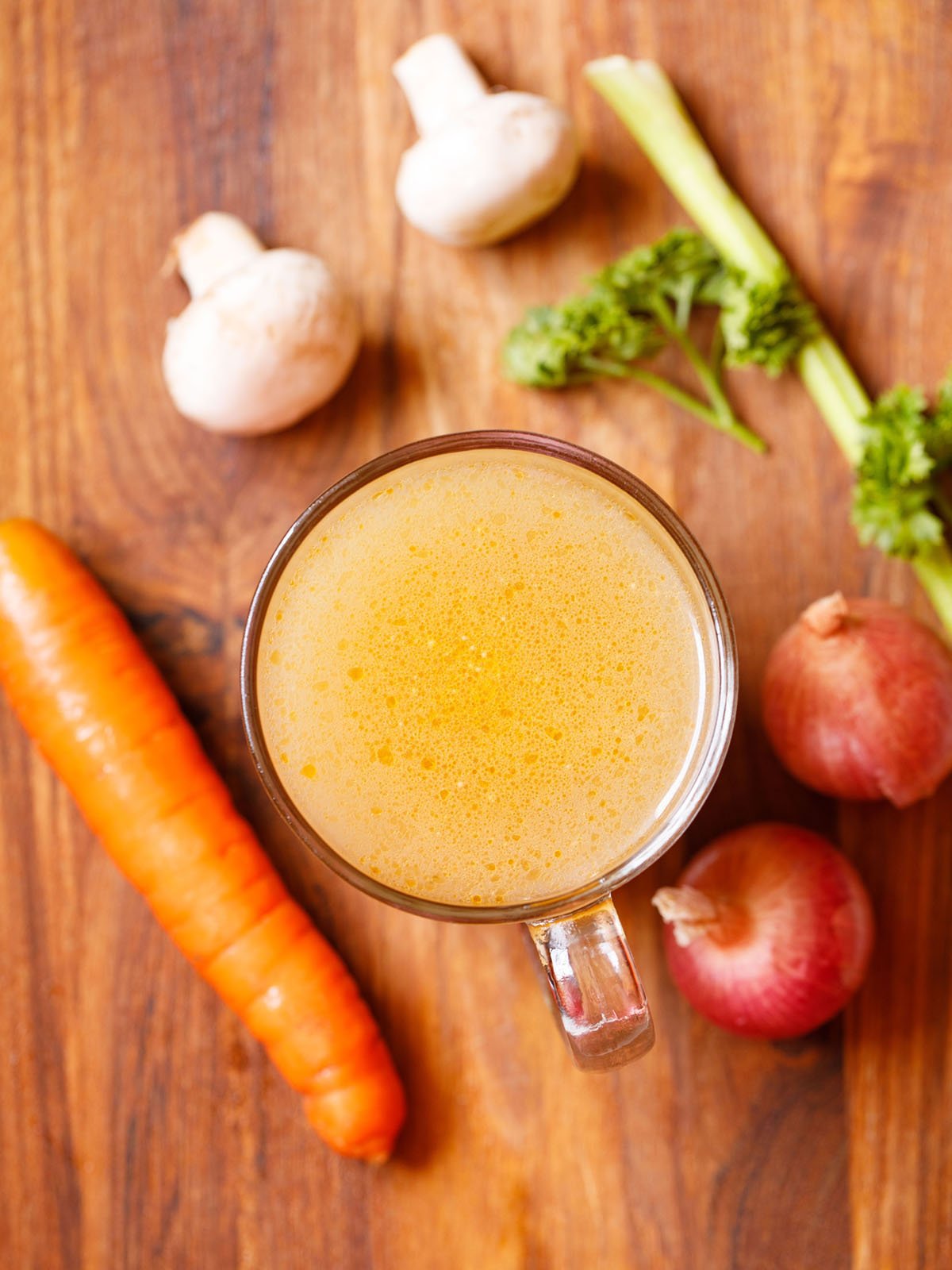 vegetable broth in a glass mug with vegetables, button mushrooms and parsley by the side