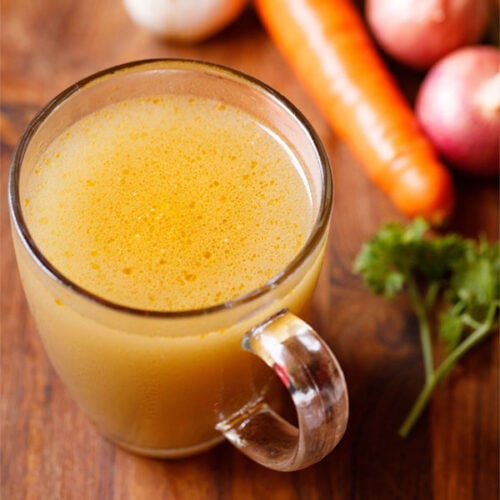 vegetable stock in a glass mug with vegetables and parsley by the side