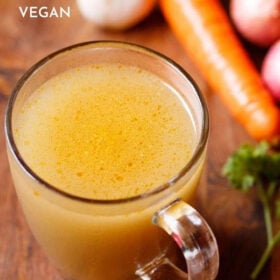 vegetable stock in a glass mug with vegetables and parsley by the side