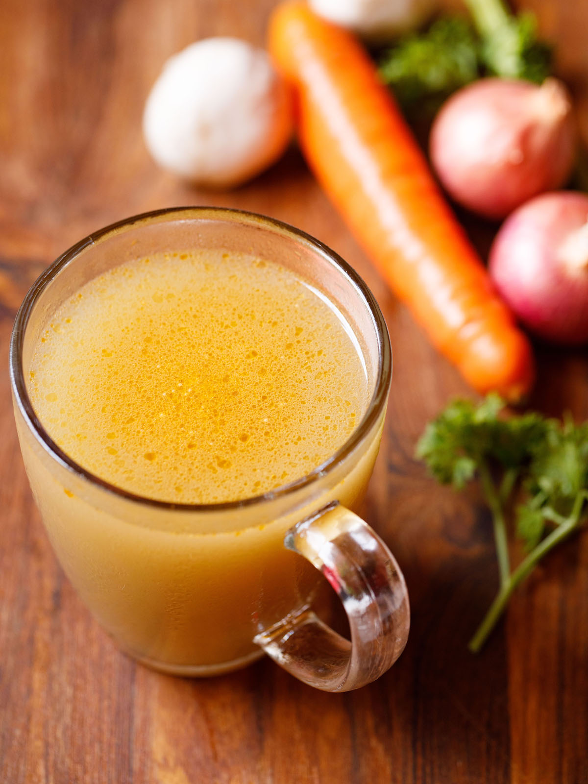 vegetable stock in a glass mug with vegetables and parsley by the side