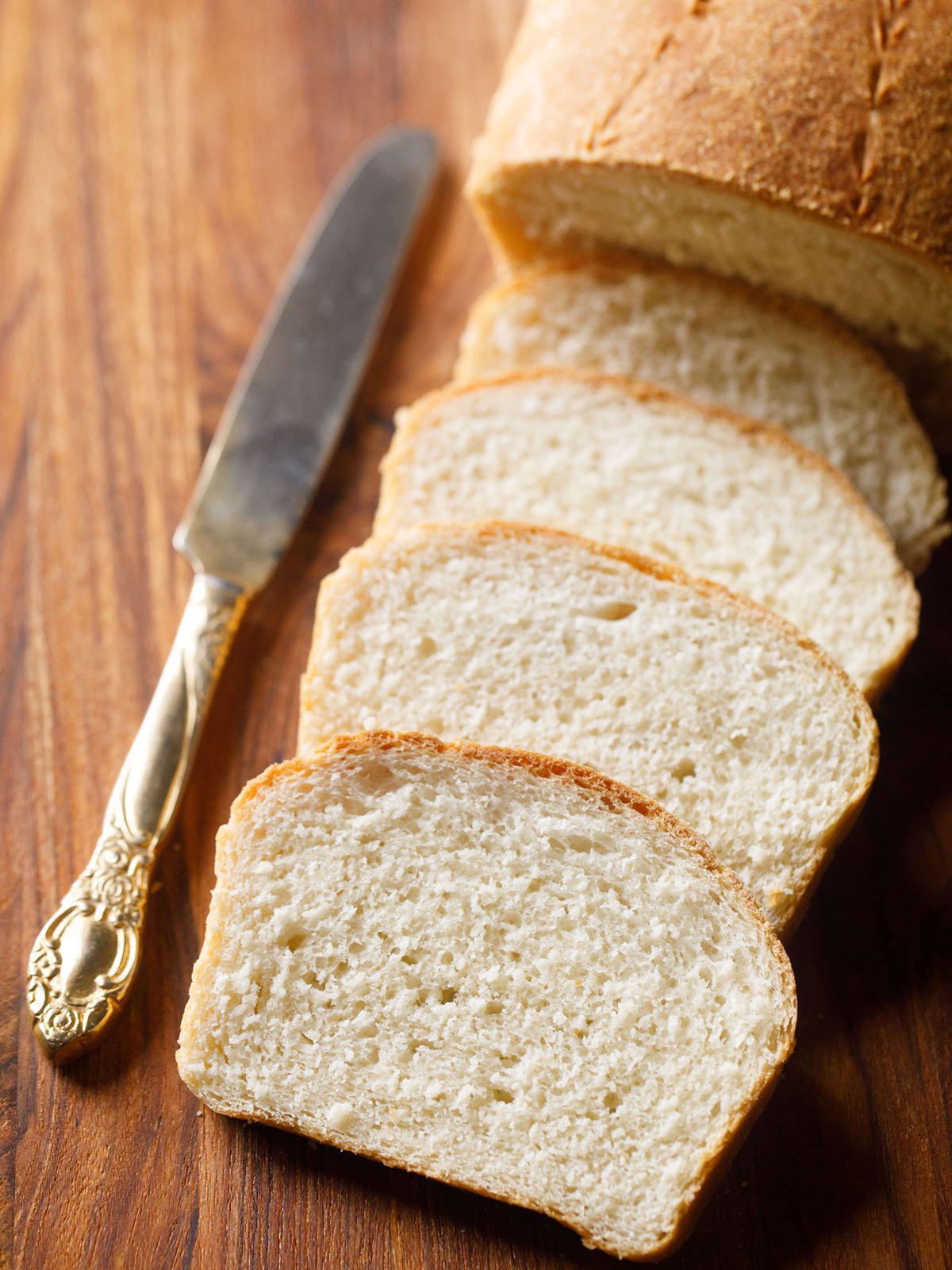 white bread loaf sliced with the slices placed on top of each other with an antique butter knife on a brown wooden board