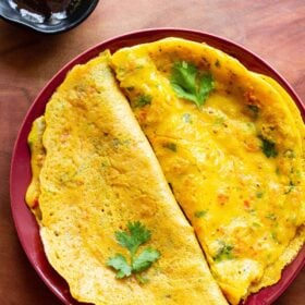 top shot of cooked and folded besan chillas on red plate with fresh herbs garnished on top