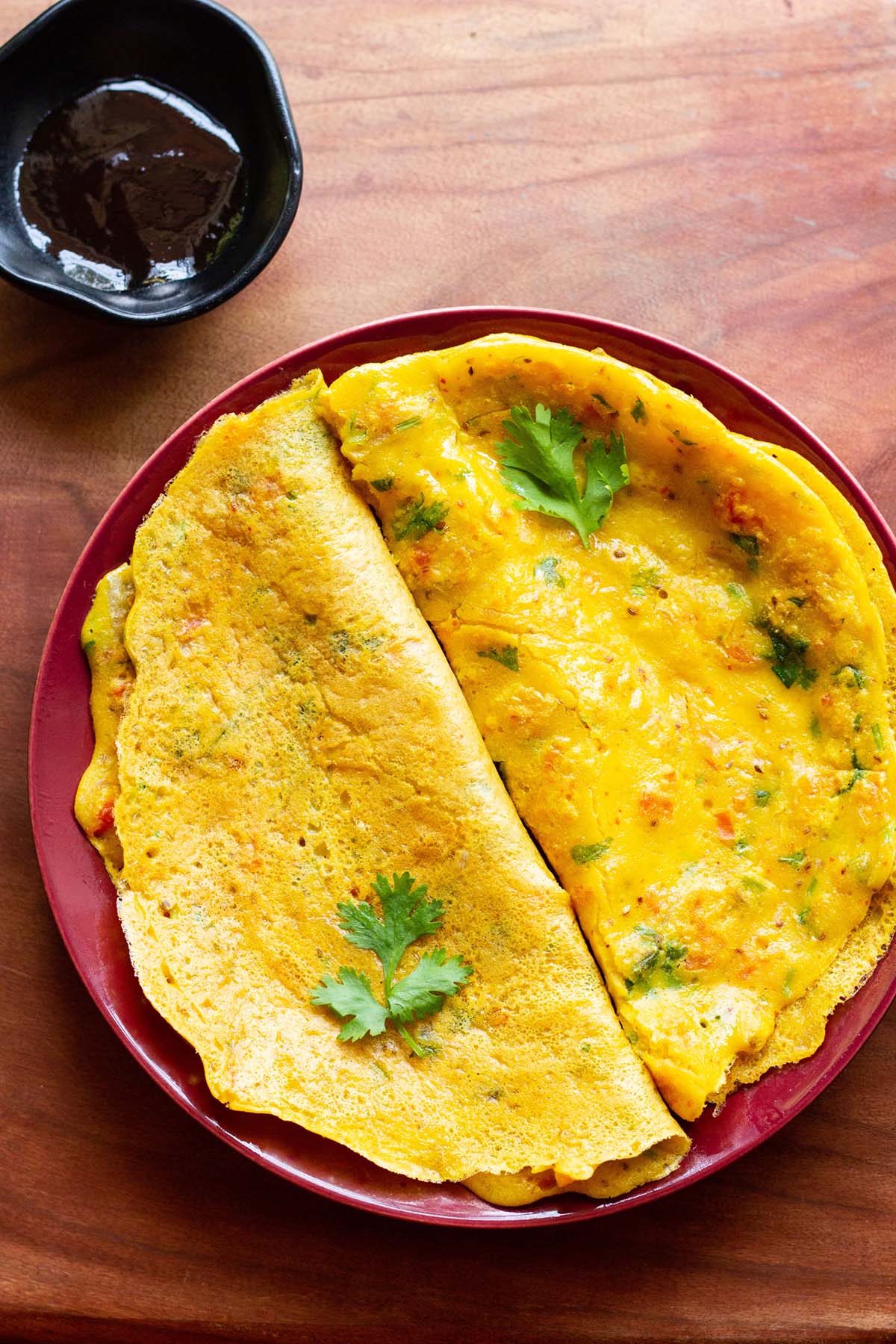 top shot of cooked and folded besan chillas on red plate with fresh herbs garnished on top