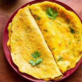 top shot of cooked and folded besan chillas on red plate with fresh coriander leaves garnished on top.