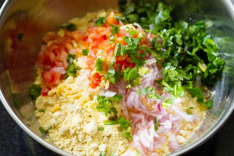 top shot of finely chopped vegetables and herbs poured onto gram flour in mixing bowl