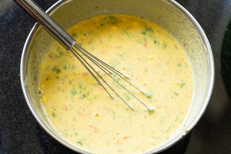 top shot of besan chilla batter in mixing bowl with wire whisk