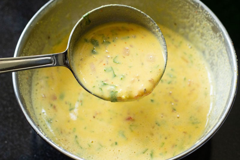 ladle scooping besan chilla batter out of mixing bowl