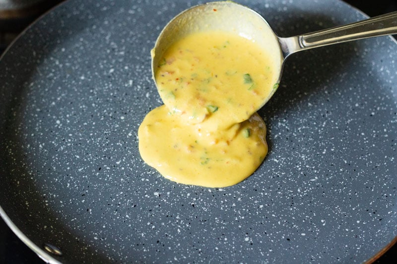 ladle pouring batter onto center of flat pan on stove