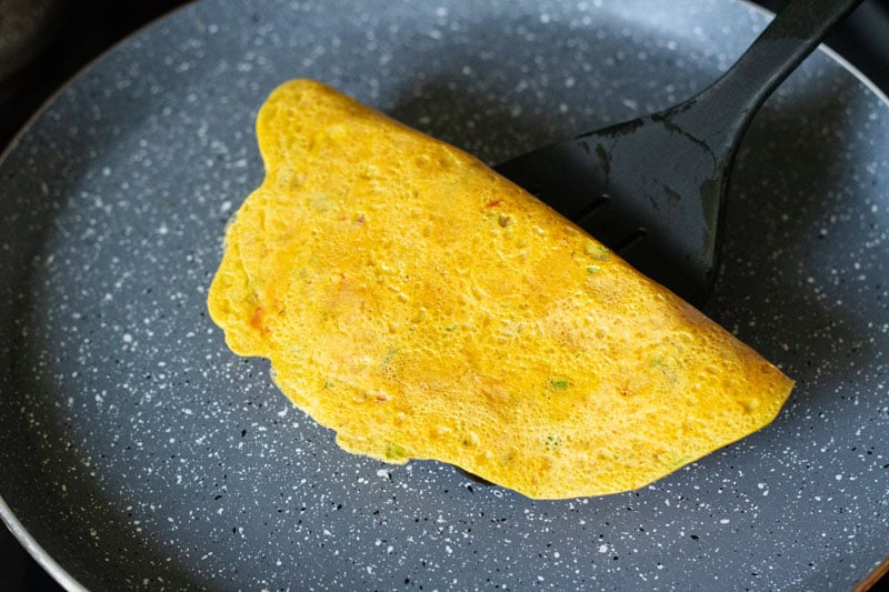 cooked and folded besan chilla being taken off of pan with spatula