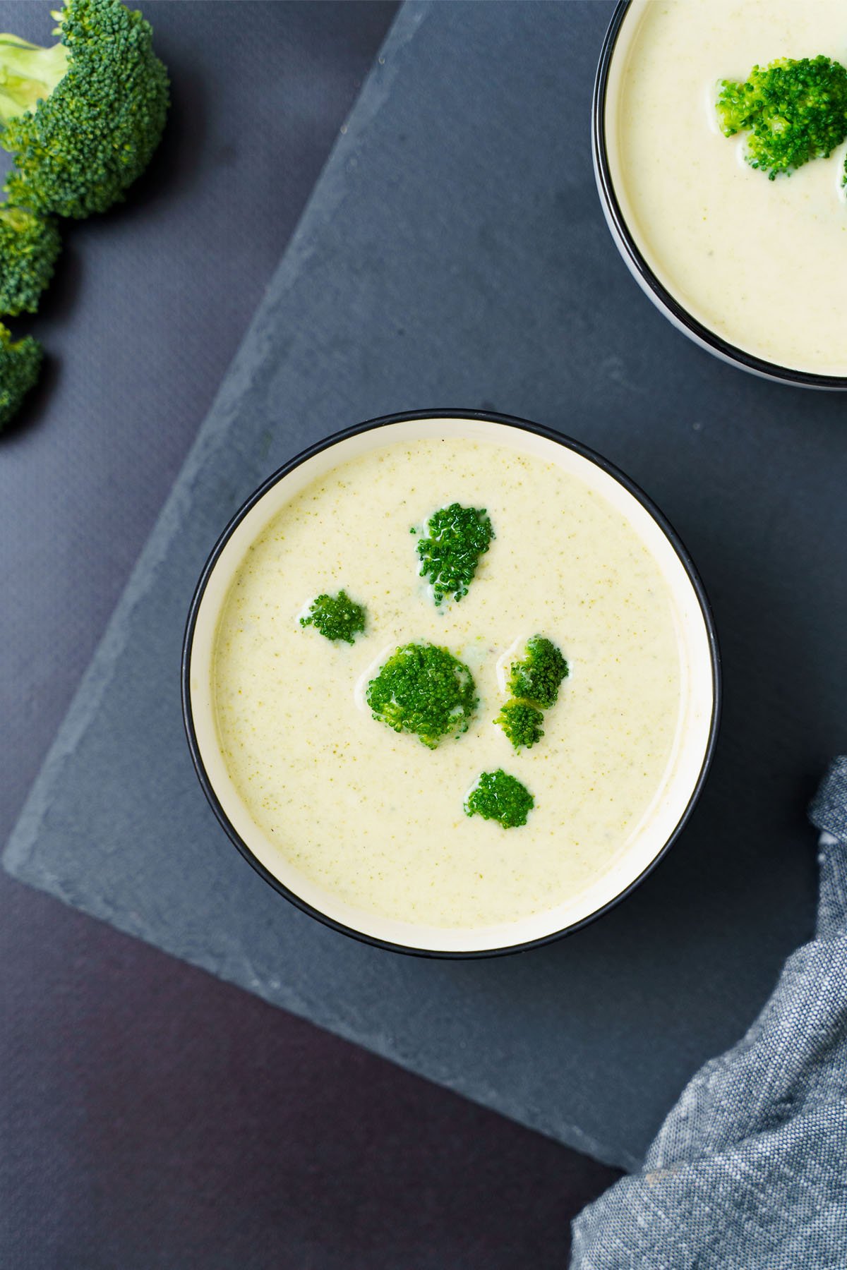 broccoli soup topped with broccoli florets in a black rimmed white bowl on a slate board