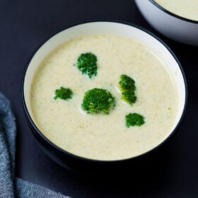 Cream of broccoli soup with broccoli florets in a black-rimmed white bowl on a black board